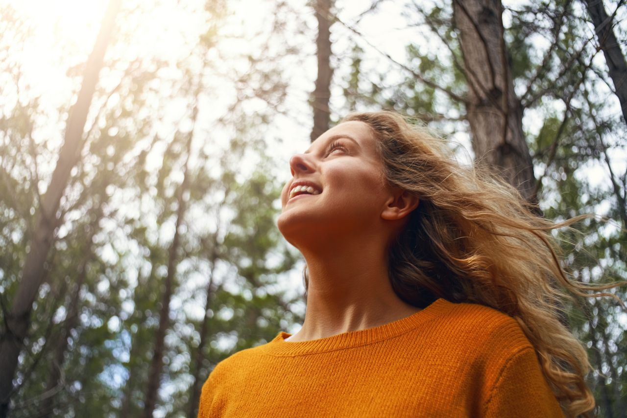 Une jeune femme souriante profite d’un moment au soleil dans une forêt