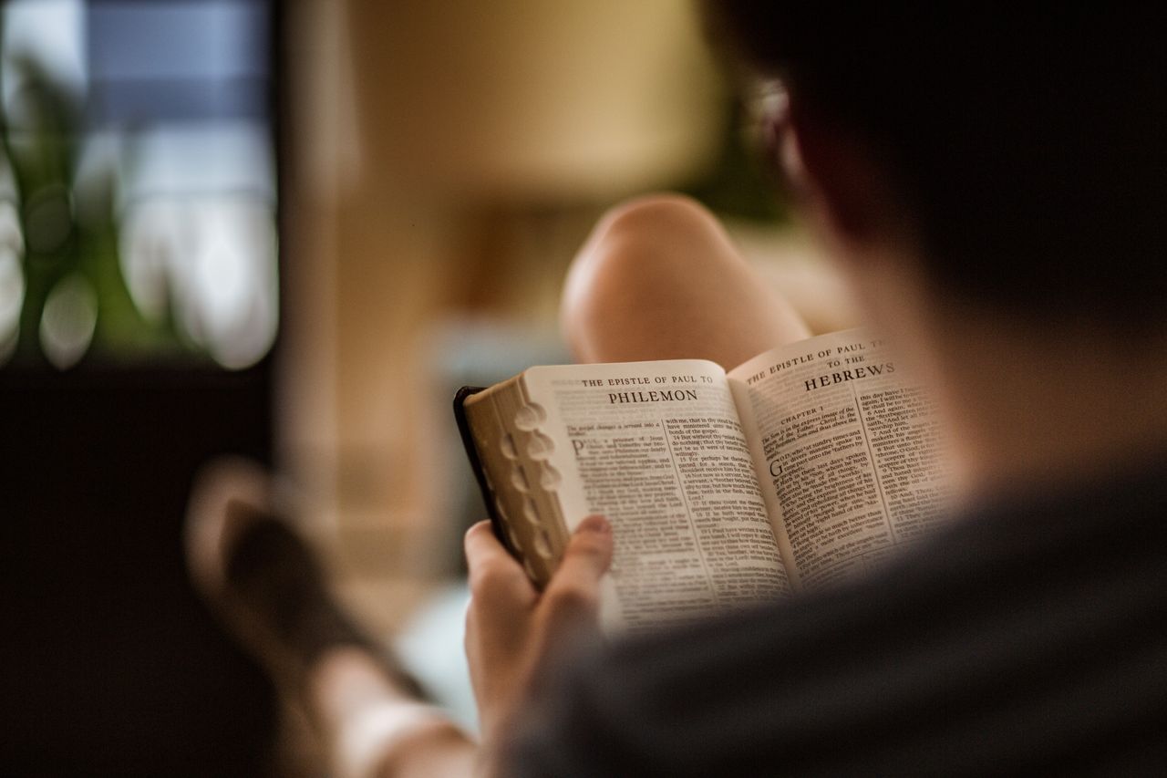 Un homme assis sur un canapé étudie la Sainte Bible, les pages ouvertes à l’épître de Paul à Philémon