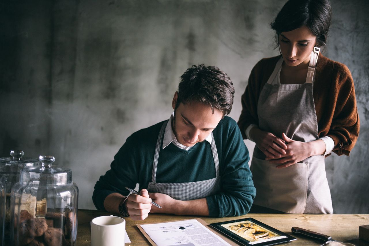 Un couple assis autour d’une table examine une recette de cuisine